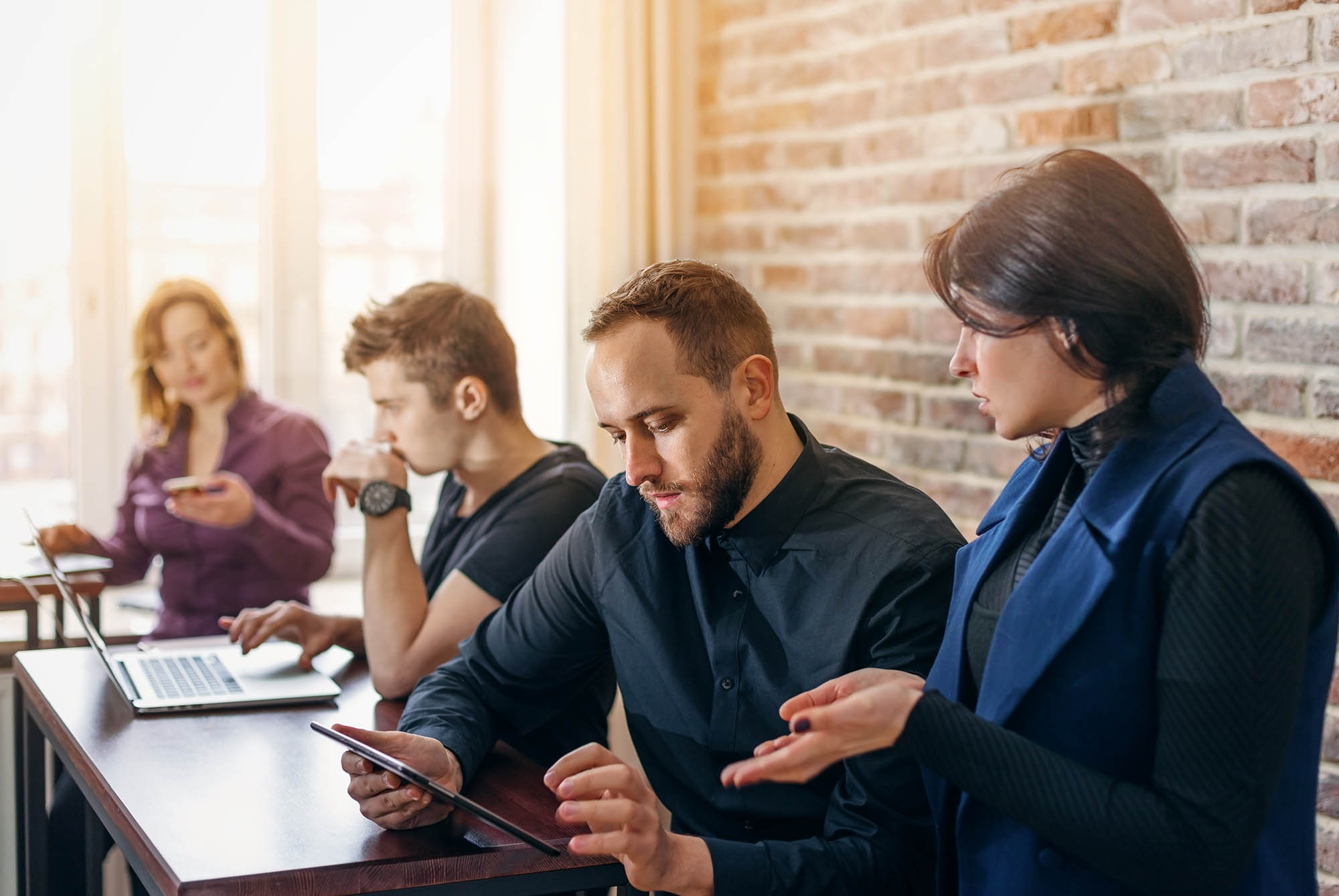 Coworkers collaborating on intercompany accounting tasks using tablet and laptop in office setting